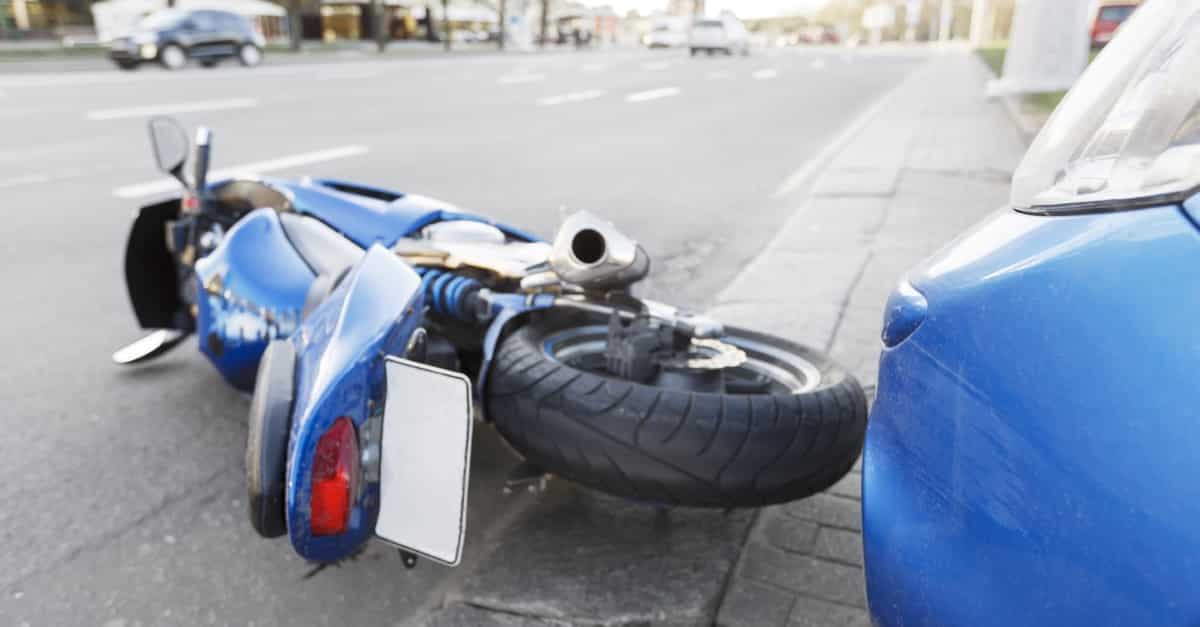A motorcycle on its side after a crash with a blue car