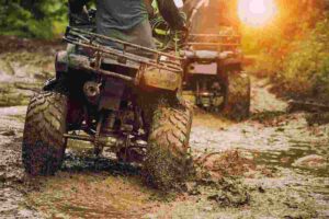 People riding ATVs through muddy terrain