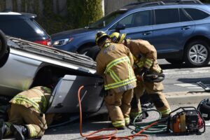 Fire fighters using the jaws of life on a flipped car after a wreck