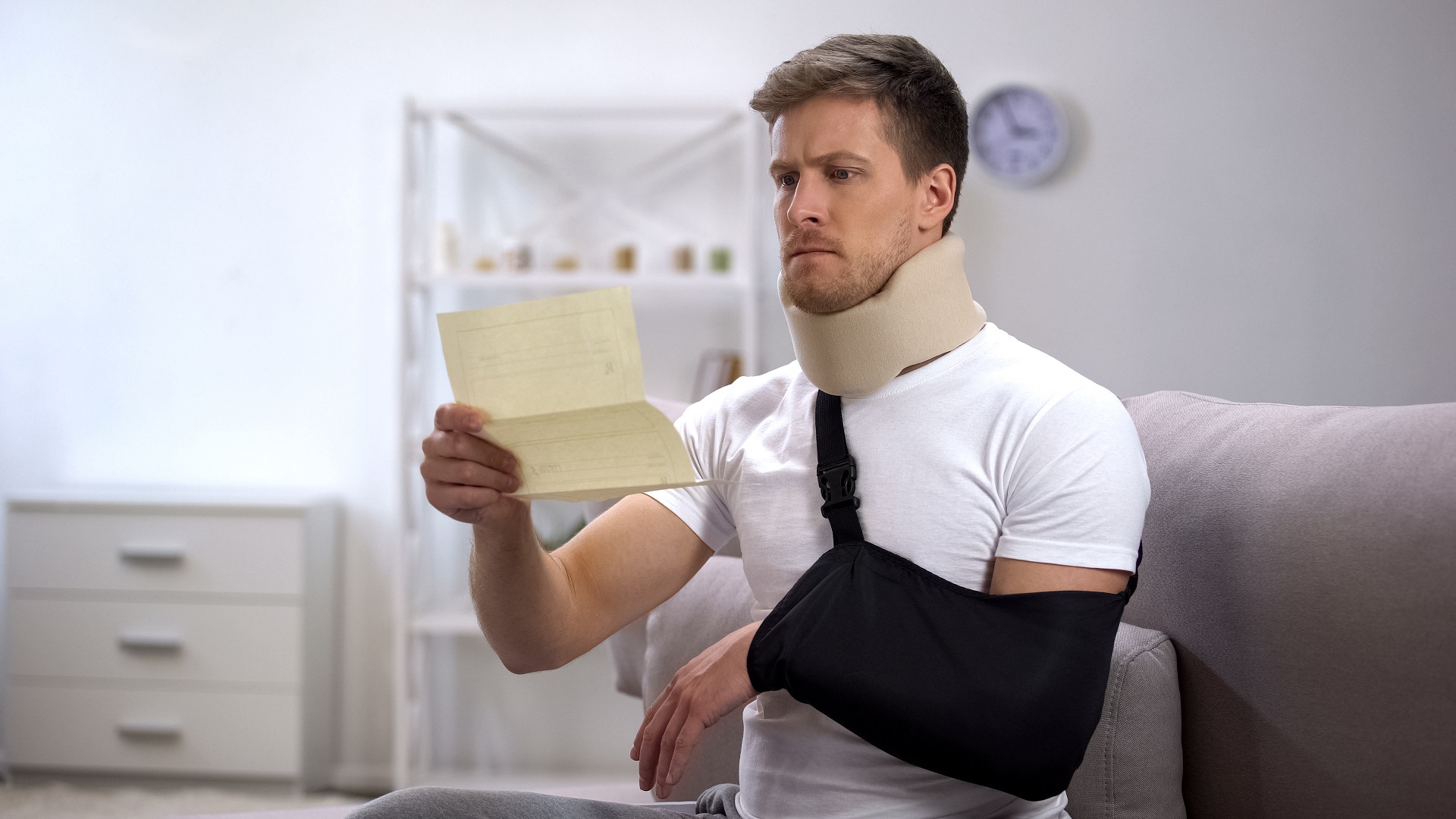 Man in foam cervical collar and arm sling reading medical bill, shocking price