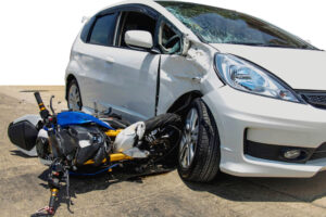 A motorcycle crashes into the side of a white saloon car, resulting in visible damage to both vehicles and highlighting the severity of the road accident.