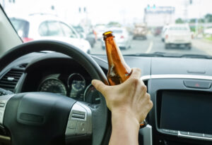 A driver grips a bottle of alcohol while behind the wheel, illustrating the concept of drunk driving. 