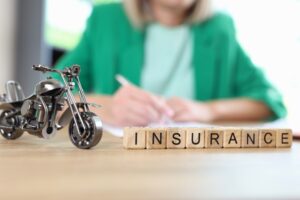 A motorcycle model and the word "insurance" are on a table, with a blurred manager handling documents in the background, emphasizing the travel and medical insurance concept.