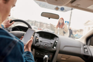 A male driver, distracted by his mobile phone, recklessly runs over a pedestrian while driving.