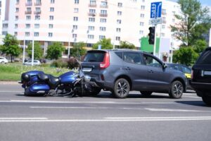 Closeup of a motorcycle colliding with the back of a car on the road.