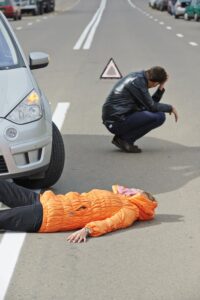 A road accident involving a pedestrian being struck, with an upset driver standing in front of the damaged vehicle after the collision.