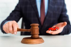 A cropped view of a lawyer holding a gavel next to a model of a car. 