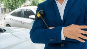 A lawyer stands beside a car, holding a gavel that symbolizes legal authority and judgment, representing legal consultation and advocacy in the scene.