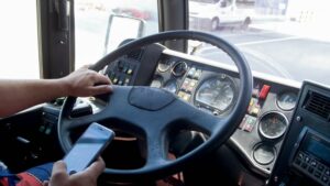 Closeup of a truck driver typing on a smartphone while driving, highlighting the danger and risk of distracted driving in transport.