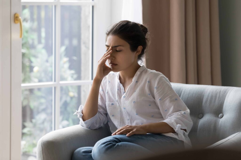 Stressed woman sitting on couch with headache, feeling emotional distress at home.