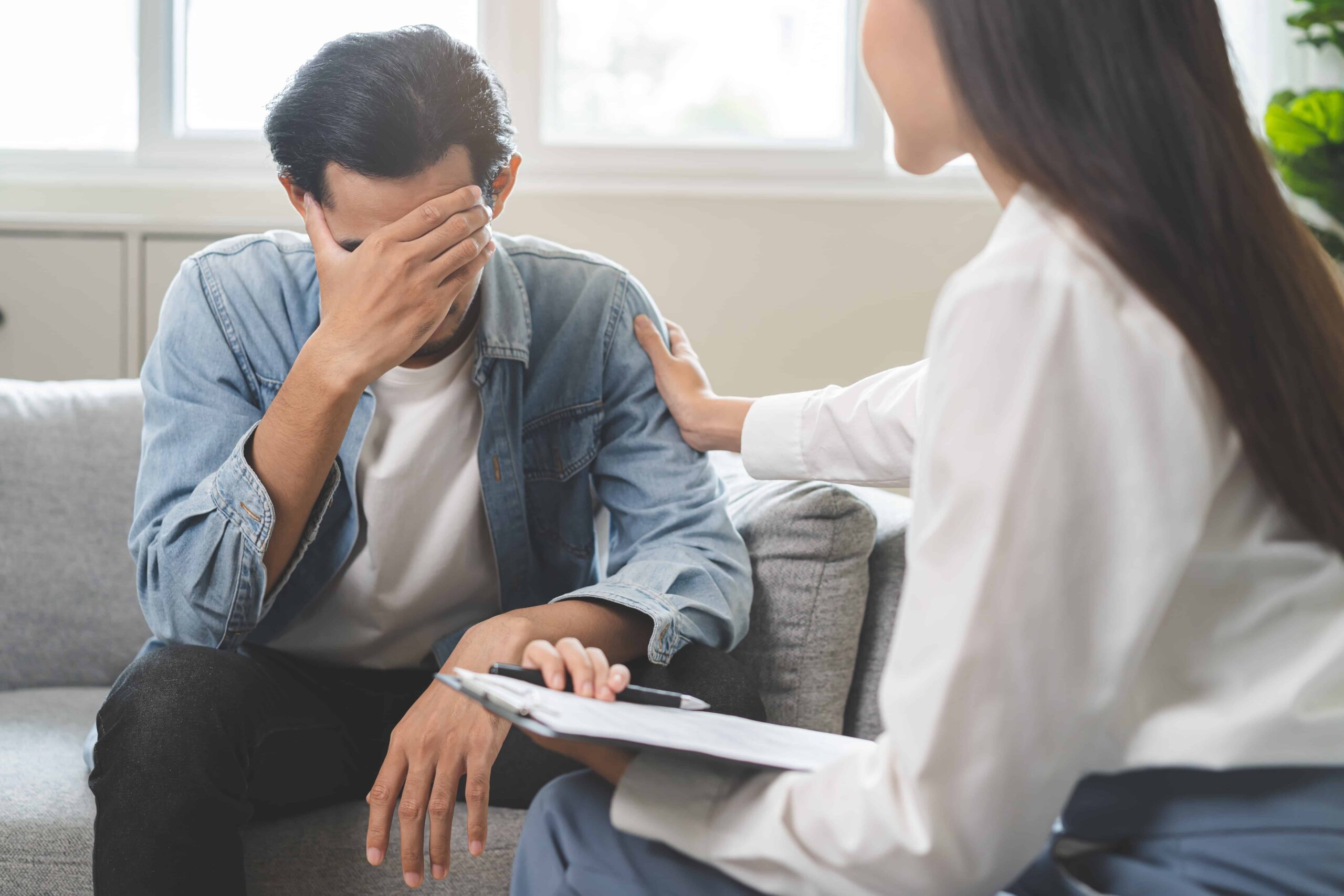 Man experiencing emotional distress during counseling session with therapist offering support.